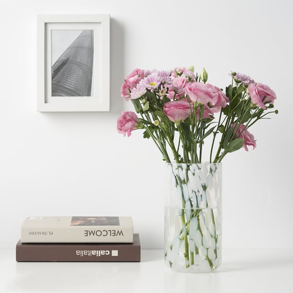 Pink flowers in HÄCKOXEL glass vase next to frames and books.