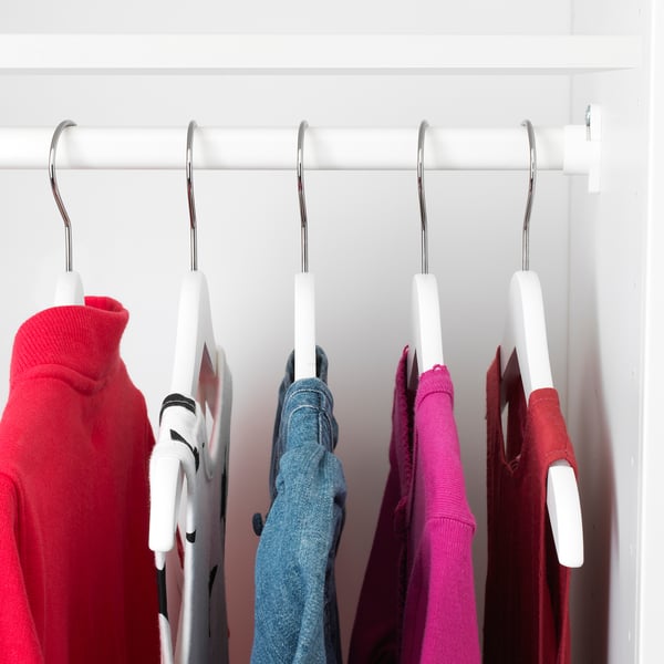 Closet with colorful kids clothes on white hangers.