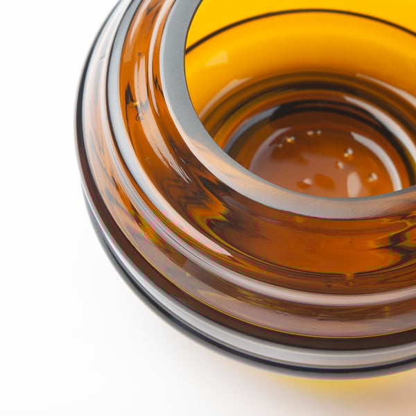 Close-up of recycled glass tealight holder, showcasing its smooth, glossy surface and warm amber hue with slight imperfections.