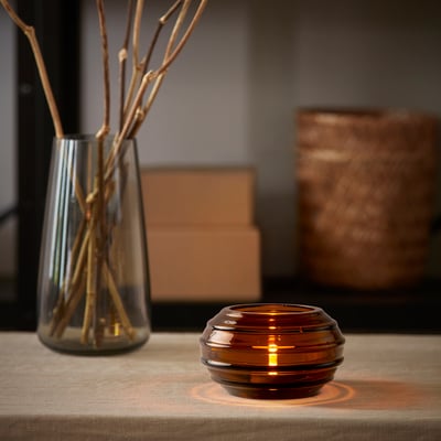 Brown glass tealight holder with dried branches in clear vase on wooden table.