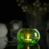 Green glass tealight holder, showing lit candle inside, casting warm light. Part of eco-friendly HÄNGBJÖRK series.