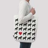 A person carrying a white tote bag with black horse patterns. A red heart is near the bottom.