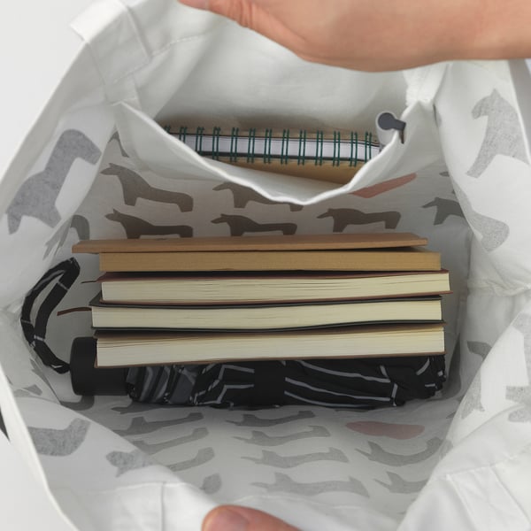 Hand holding open HÄSTHAGE bag revealing inside pocket with notebook and stacked books, showcasing storage capacity.