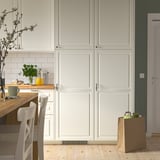 Modern kitchen with white cabinets, light wood chairs, countertop flowers, and shopping bag.