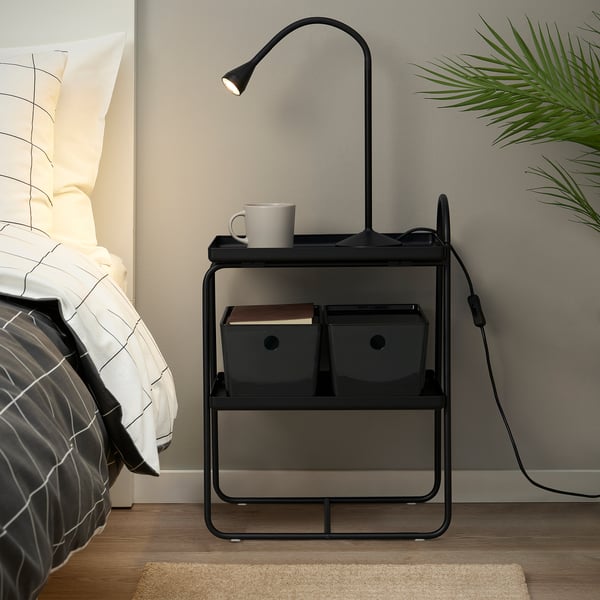 Bedside table with adjustable light, holding mug, book, and storage bins.
