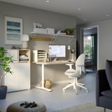 Home office with modern desk, chair, shelves, computer, lamp, plants, bookcase, and painting.