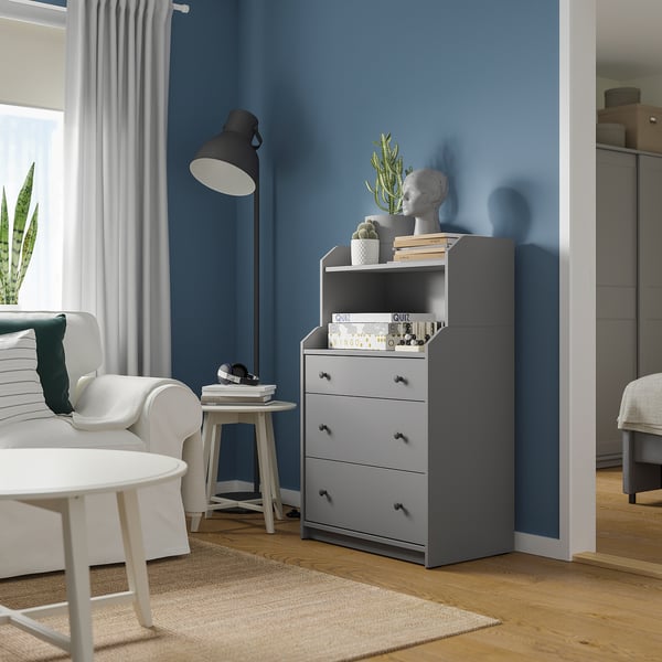 Modern living room with white couch, black lamp, grey HAUGA chest of three drawers and top shelf against blue wall.