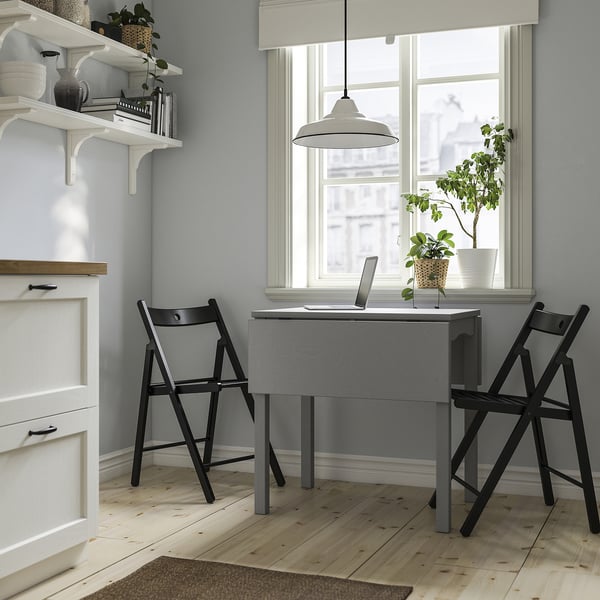 Compact home office with HAUGA table, two chairs, shelves, and large window.