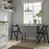 Compact home office with HAUGA table, two chairs, shelves, and large window.