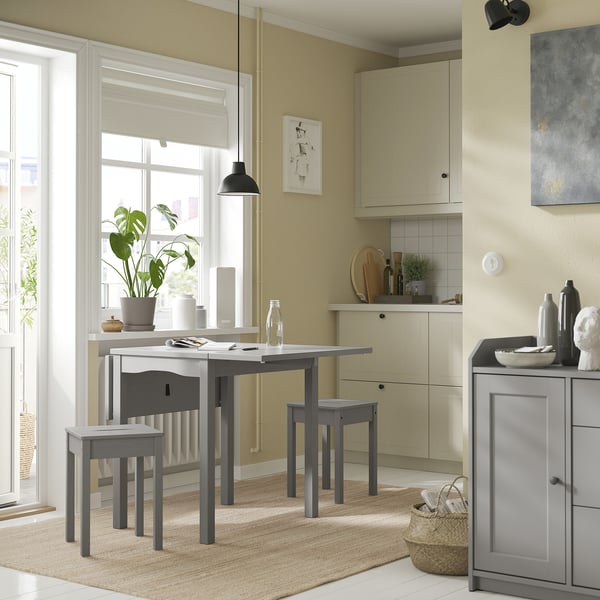Cozy kitchen nook with HAUGA grey drop-leaf table and stools, beige rug, and potted plant.