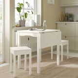 Small white kitchen setup, featuring HAUGA drop-leaf table and stools in bright, natural wood finish.