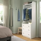 Bedroom with white HAUGA dresser, hanging clothes, mirror, bed, and wooden floor.