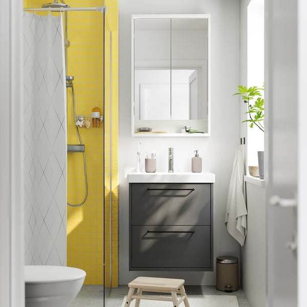 Modern bathroom dark grey HAVBÄCK vanity, bright yellow shower tiles. Sink and mirror combo, trousers on door.