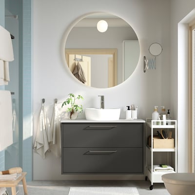 Modern bathroom with HAVBÄCK vanity, mirror, sink, grey cabinets, minimalist handles, shelf, and plant. Clean atmosphere with hanging towels.