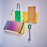 A yellow HAVREKROSS wall organizer with a smartphone, keys, and notes on a light purple wall.