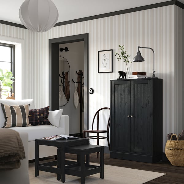 Modern living room with striped walls, featuring a black HAVSTA cabinet, white sofa, black coffee table, wicker chair, and hanging lamp.