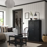 Modern living room with striped walls, featuring a black HAVSTA cabinet, white sofa, black coffee table, wicker chair, and hanging lamp.