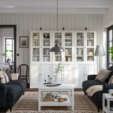 New living room: HAVSTA white pine bookshelves, gray couches, black pendant light, patterned rug, coffee table with decor and pillows.