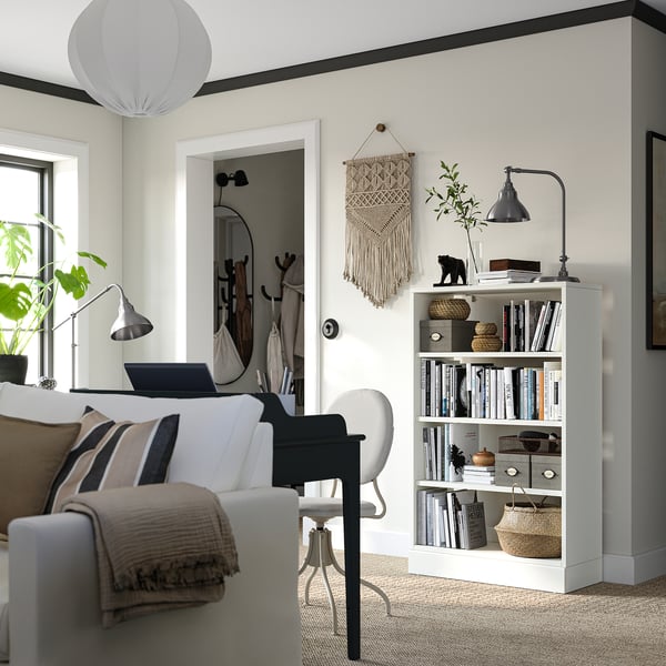 Bright living space with modern decor: white sofa, gray chair, wooden bookshelf with books, plants, and a black lamp.