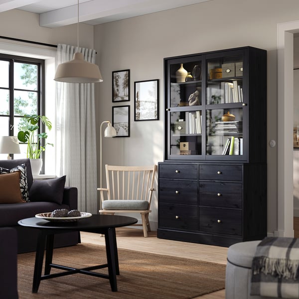 HAVSTA display & chest in modern living room with books, vases, grey couch, wooden chair, and large window.