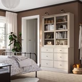 Cozy bedroom with HAVSTA bed, white bedding, light brown cabinet & chest, books, and large plant.
