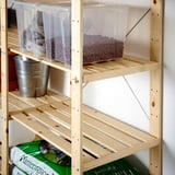 Wooden storage shelves with clear plastic containers holding small brown spherical items, and a green bag below.
