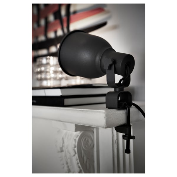 Black adjustable clamp lamp attached to white surface, directing light.