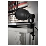 Black adjustable clamp lamp attached to white surface, directing light.