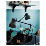 Modern bedroom with black adjustable HEKTAR lamps, one on a wall shelf and another on a desk beside a blue mirror and vase with flowers.