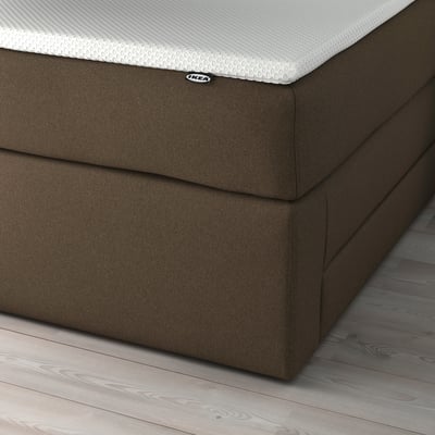 Close-up of HEMFJÄLLET bed showcasing two large storage drawers under a gray upholstered bed base with a white textured mattress.