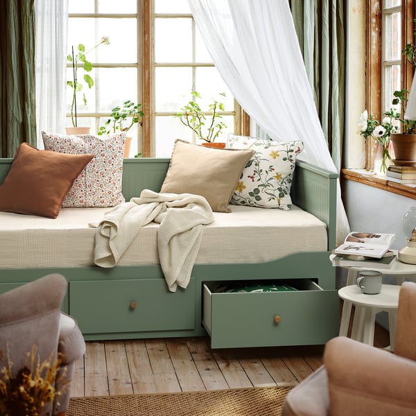 Day-bed transforms from sofa to bed, includes storage. Soft pillows and blanket, with plants nearby.