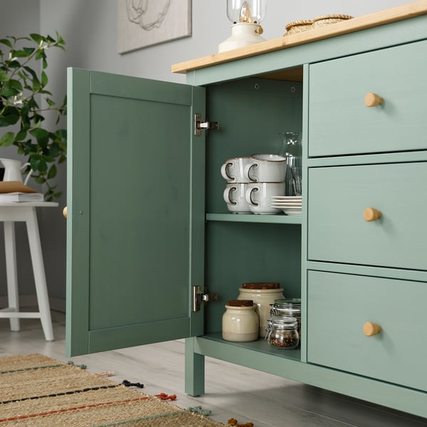 Green HEMNES sideboard with open door displaying cups, plates, and jars on shelves, showing storage and organisational.