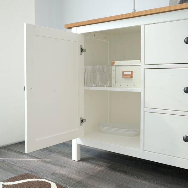 White HEMNES sideboard with one door open, revealing glassware and dinnerware stored inside. Display shelf on top.