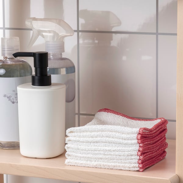 Shelf with soap dispenser and stacked white towels with red trim.
