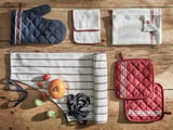 Kitchen cloth set: blue, white, red cotton; includes oven mitts, towels, dishcloths on wood; tomatoes, garlic.
