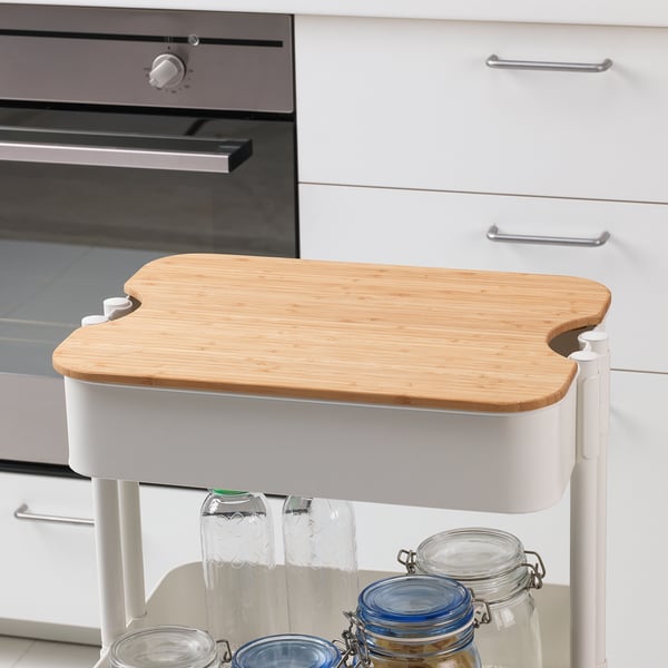 Bamboo cutting board as lid on container near oven and cabinet.