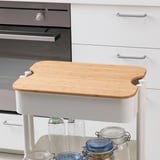 Bamboo cutting board as lid on container near oven and cabinet.