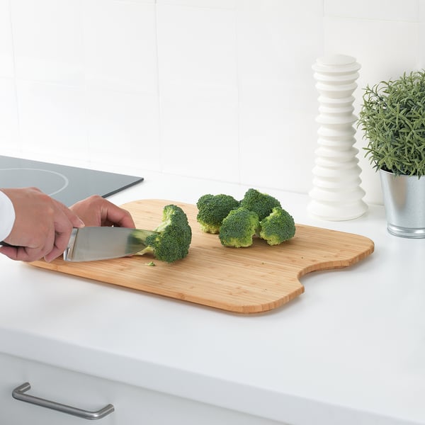 Person cutting broccoli on HÖGSMA bamboo chopping board on kitchen counter. Board has a non-slip grip.