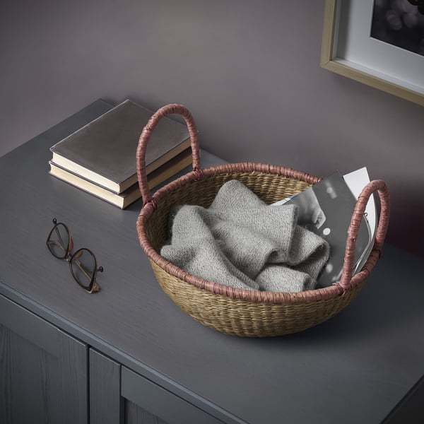 Wicker basket holding neatly folded grey blanket next to a stack of books on a dark wood surface.