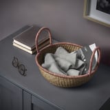 Wicker basket holding neatly folded grey blanket next to a stack of books on a dark wood surface.