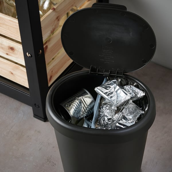 Black trash bin with lid open, showing crumpled aluminum foil inside, designed for waste sorting and cleaning efficiency.