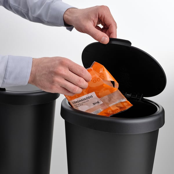 Person disposing orange-signed waste into HÖLASS sorting bin with lid open.