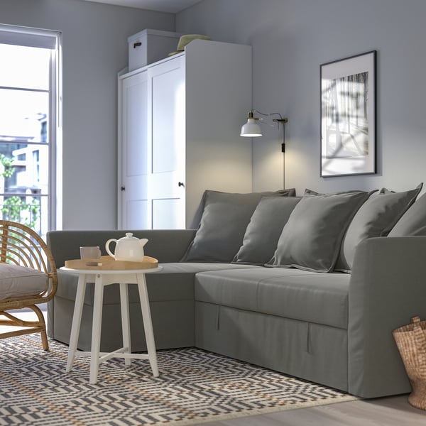 Modern living room with HOLMSUND sectional sofa, white table, cabinet, and lamp.
