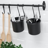 Black hanging kitchen utensil holders with wooden spoons and metal utensils in a white-tiled kitchen.