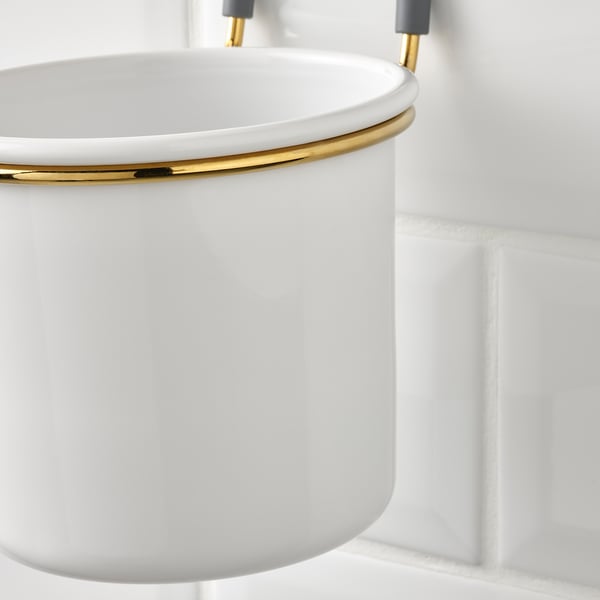 A hanging kitchen bowl, white with a gold ring, attached to a gray hook on a rail.