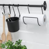 Black HULTARP rail mounts on white brick wall, holding black container with utensils and white paper towel roll.
