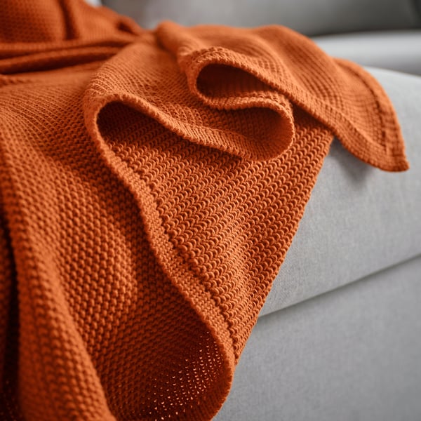 Soft, textured orange throw blanket draped on a white surface.