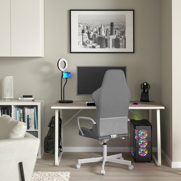 Modern gaming setup with HUVUDSPELARE gray desk, ergonomic gray chair, large monitor, ring light, bookshelf, city art, and computer tower.