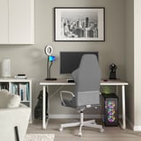 Modern gaming setup with HUVUDSPELARE gray desk, ergonomic gray chair, large monitor, ring light, bookshelf, city art, and computer tower.