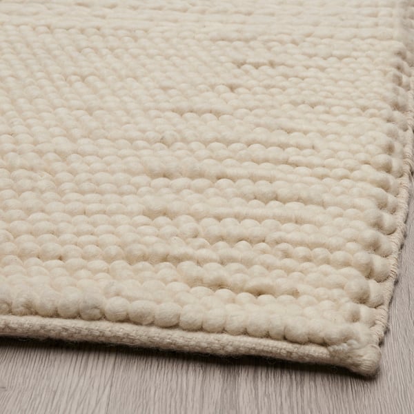Textured, beige woven rug on a wooden floor. Intricate patterns and high-quality craftsmanship.
